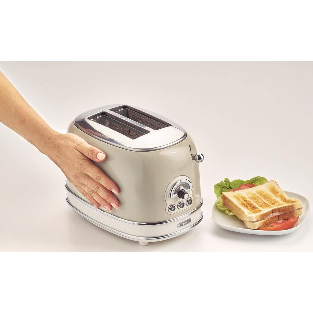 Een hand raakt een licht beige broodrooster aan, ernaast een bord met toast en salade.