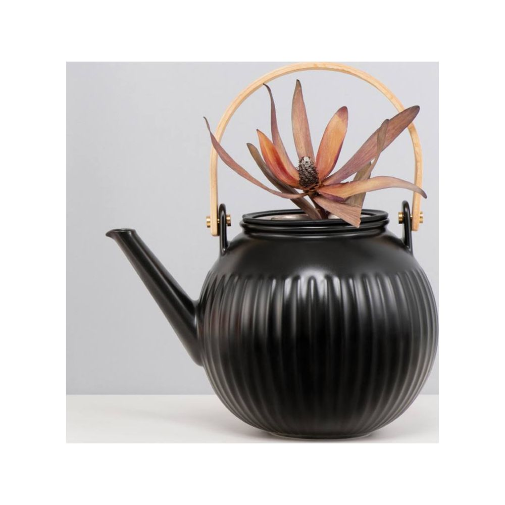 Una tetera negra acanalada con asa de madera sostiene una flor seca de color marrón anaranjado.