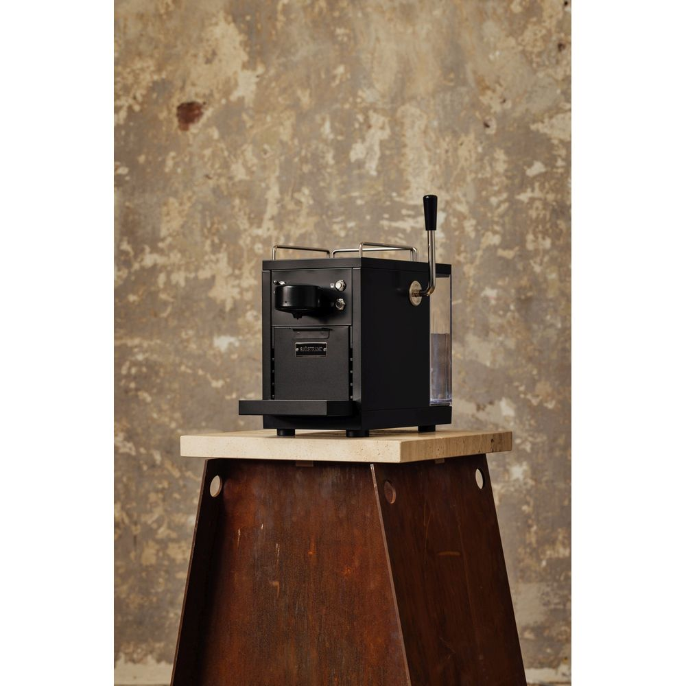 Eine schwarze Kaffeemaschine mit silbernem Hebel und Wassertank auf einem Holztisch.