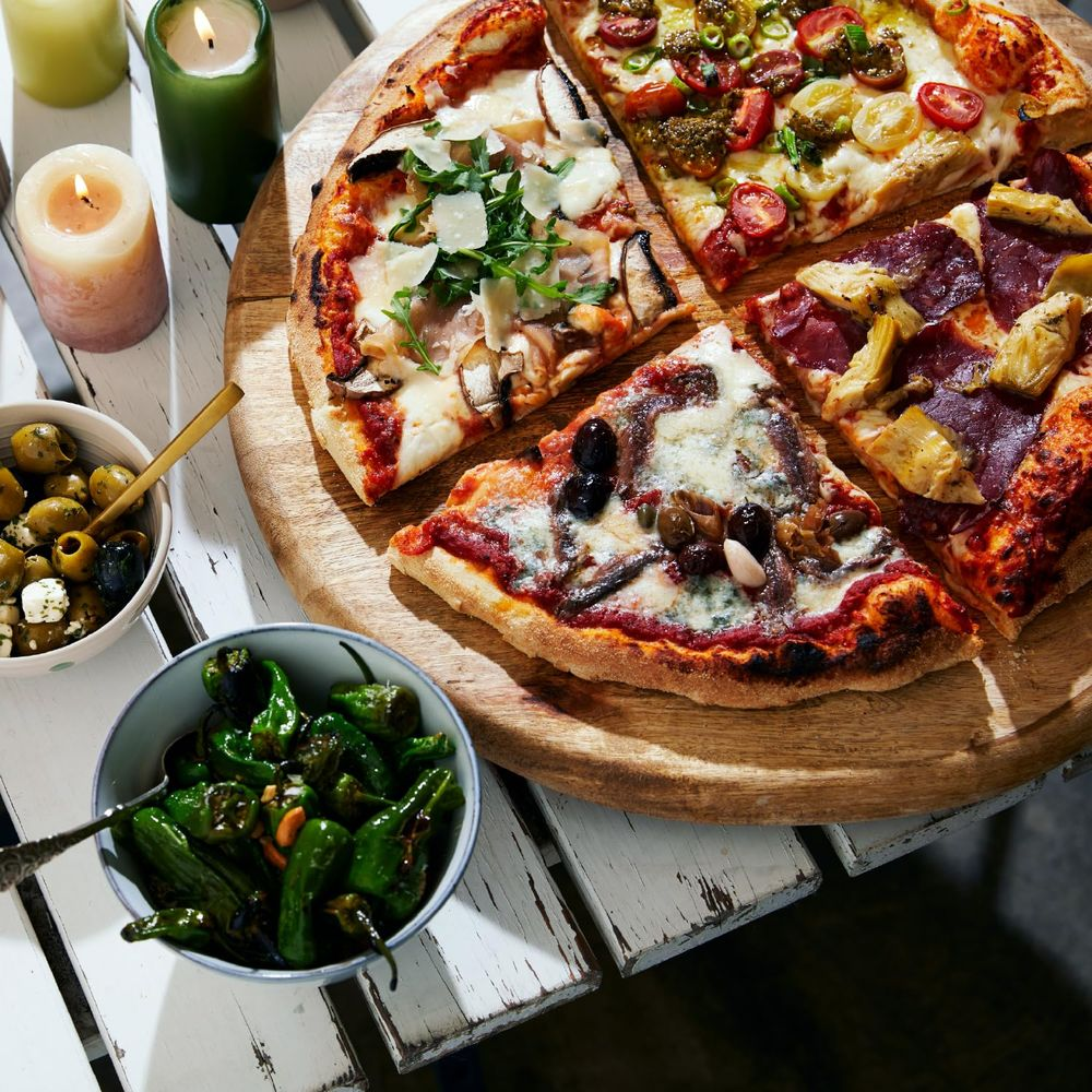 Ein Holztisch mit Pizzen, Oliven, Peperoni und Kerzen.
