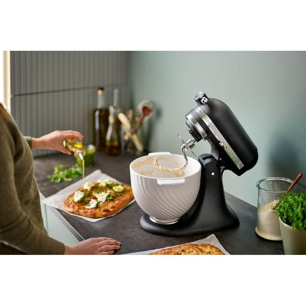 Czarny robot kuchenny z misą, obok leżą pizze.