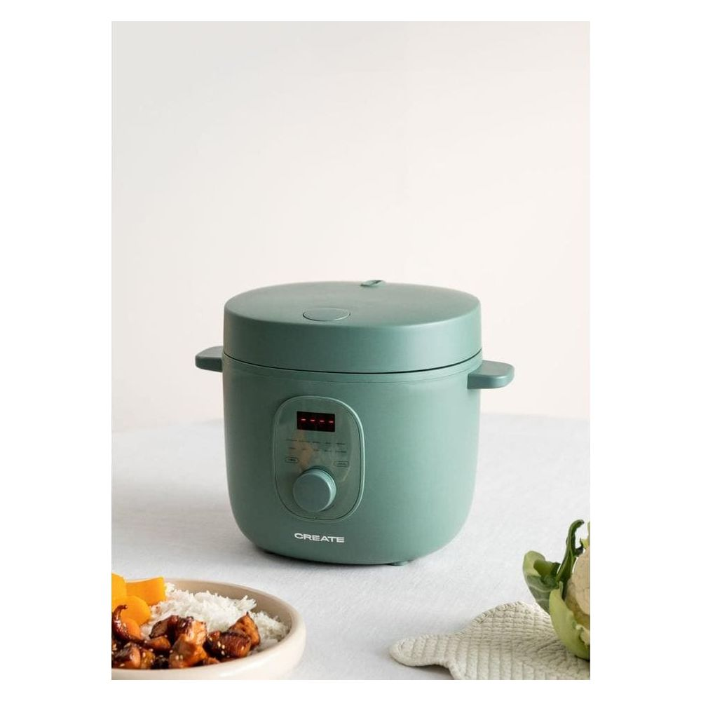 Una multi-olla verde azulado con pantalla digital sobre superficie blanca. Al lado, un bol con arroz y pollo.