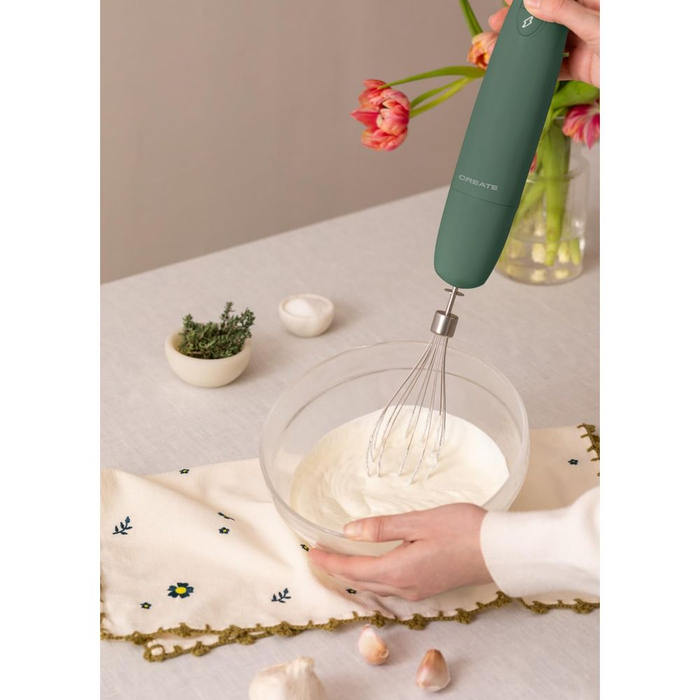 Un batidor verde de batidora de mano en un bol con crema.