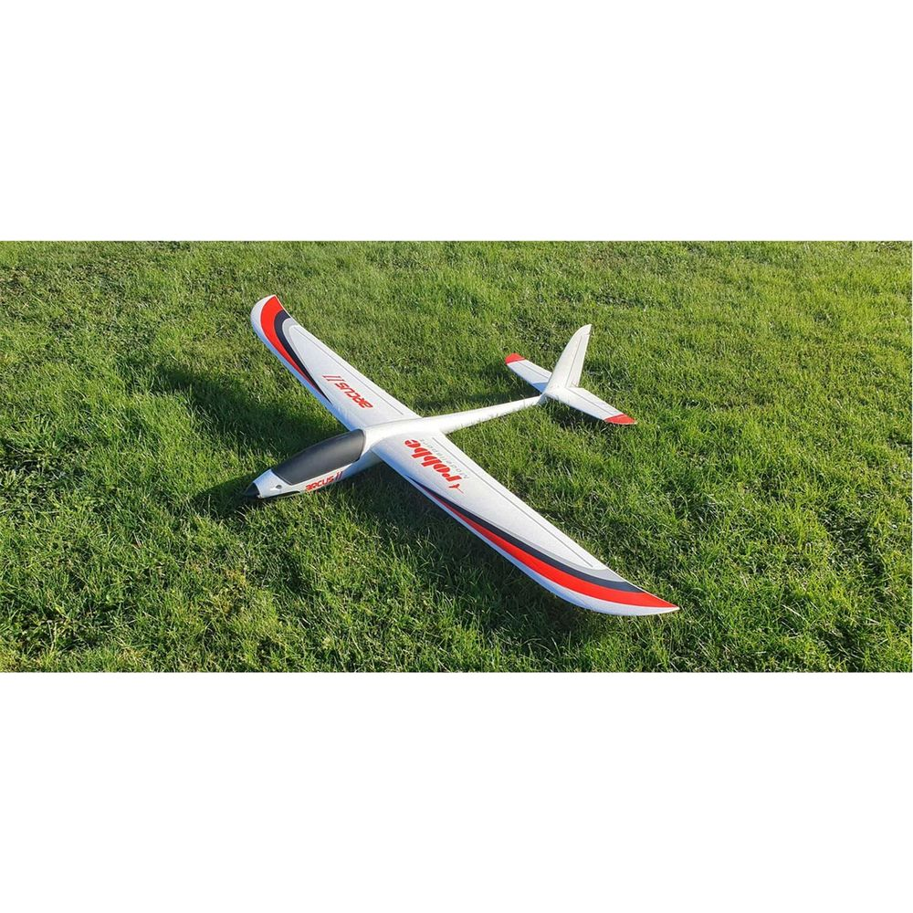 Un avion modèle radiocommandé blanc avec des accents rouges repose sur de l'herbe verte.