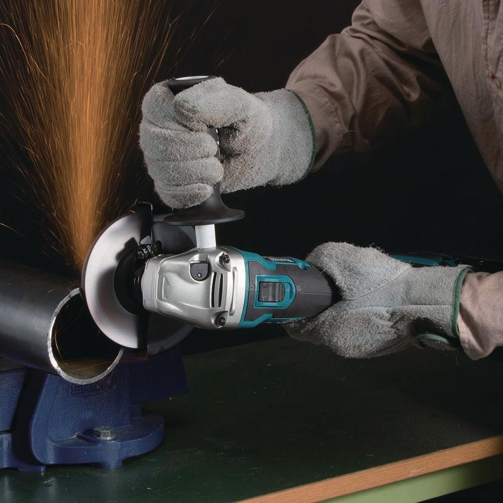 Une personne portant des gants utilise une meuleuse d'angle pour couper un tuyau métallique.