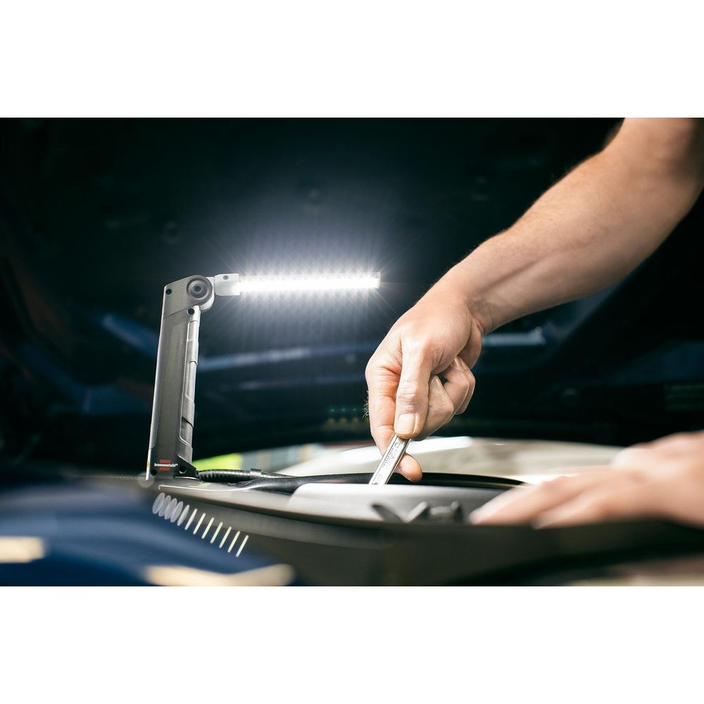 Mechaniker benutzt Schraubenschlüssel unter hellem LED-Licht im Motorraum.