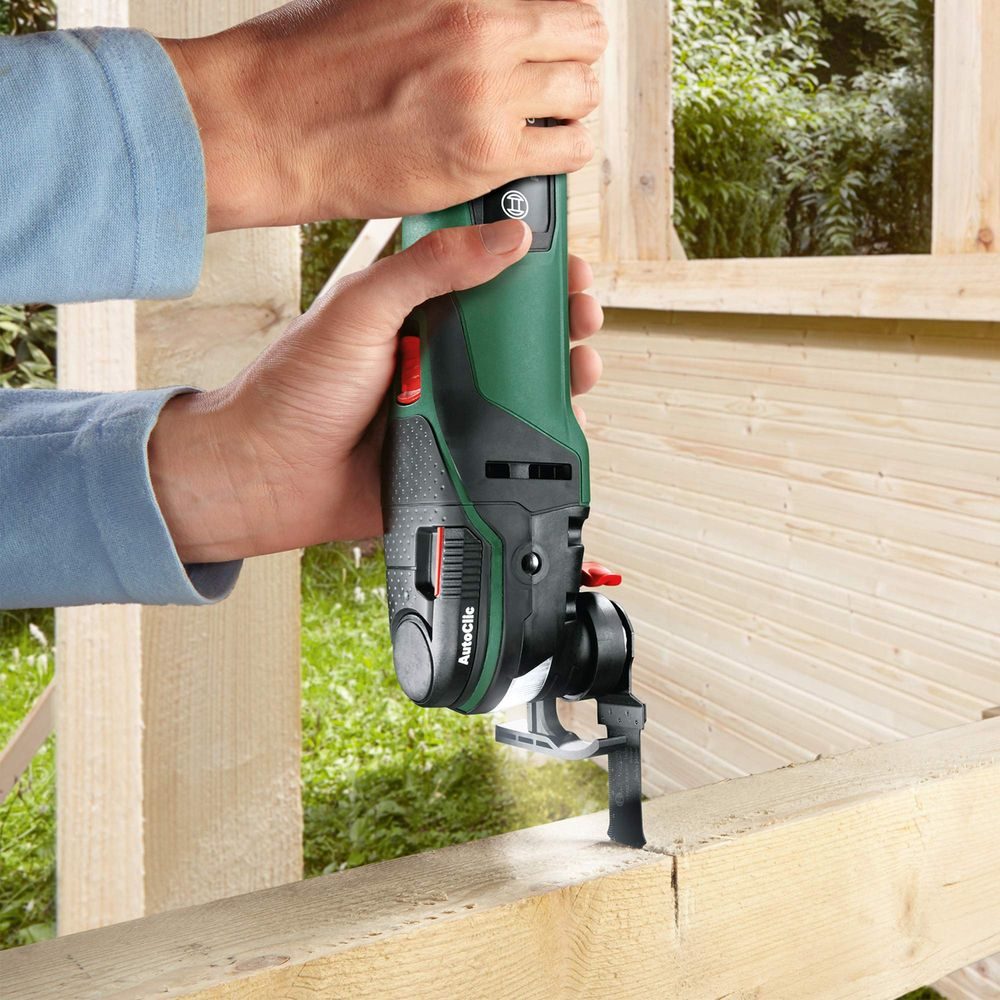 Person bearbeitet Holz mit einem grünen Multitool. Draußen, sonnig.