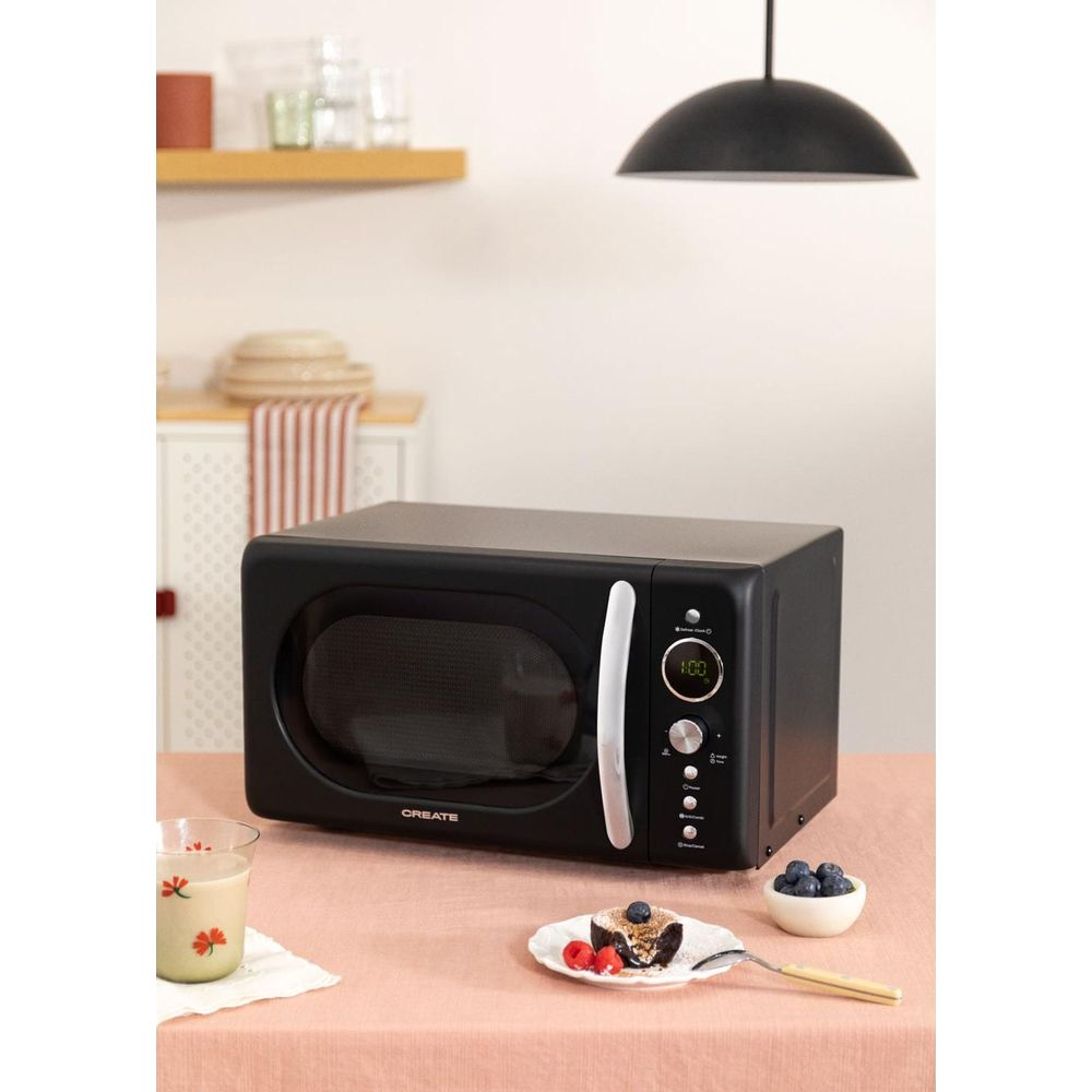 Micro-ondes noir sur table rose avec gâteau, myrtilles et verre.