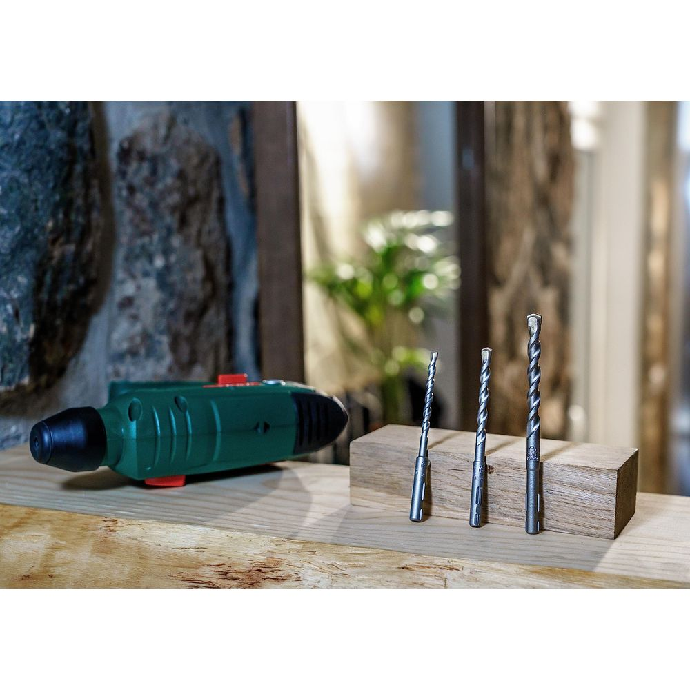 Ein grüner Bohrhammer mit drei Bohrern auf einem Holzbrett.