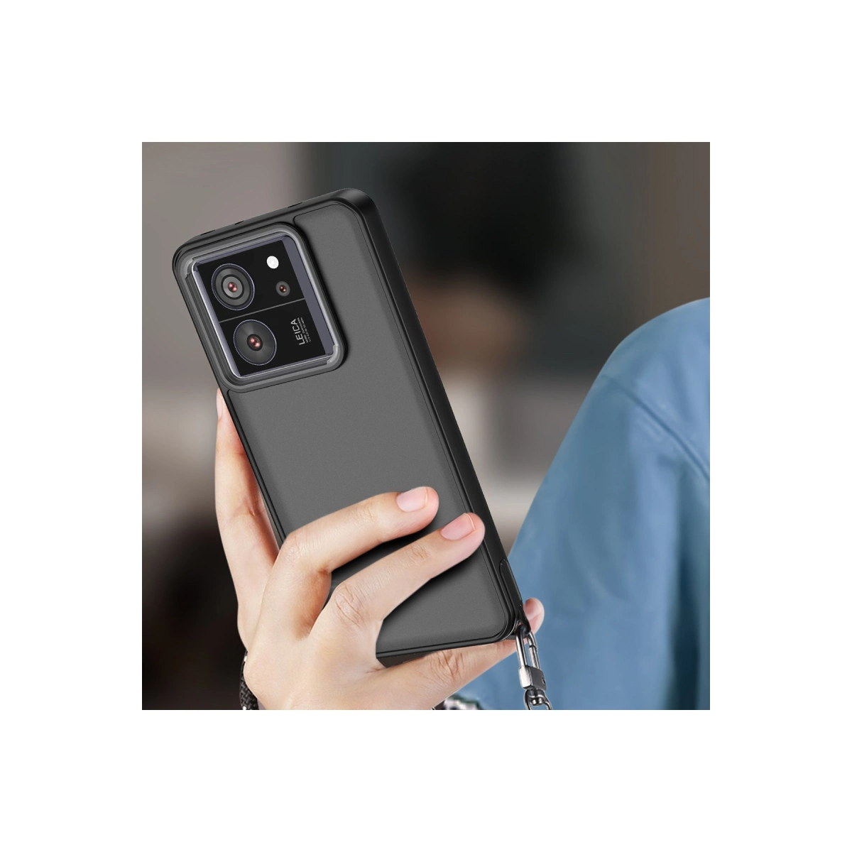 Bir el, Leica kameralı siyah bir telefon tutuyor. Bir kayış takılı.
