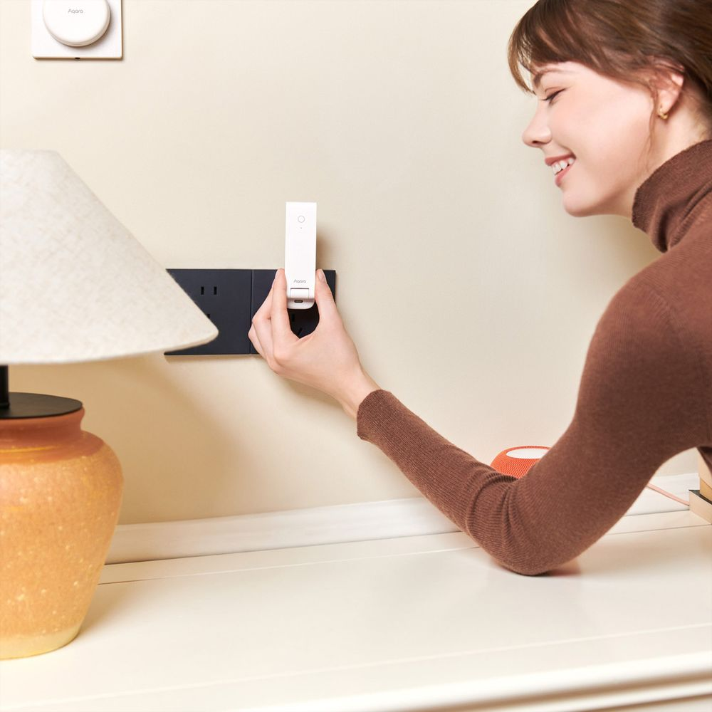 Frau steckt ein weißes Smart-Home-Gerät in eine Steckdose an der Wand.