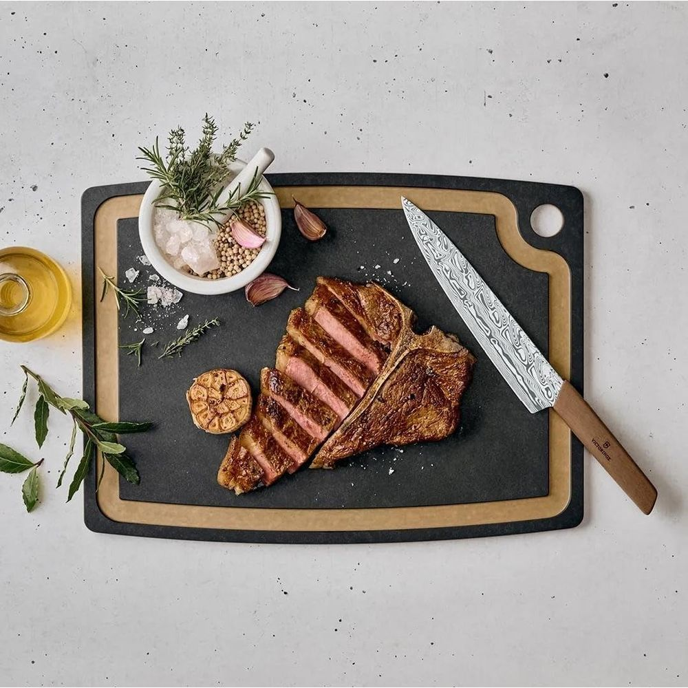 Ein geschnittenes T-Bone-Steak mit Kräutern, Knoblauch und einem Messer auf einem Brett.