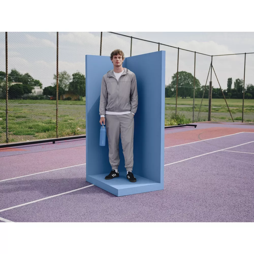 Ein Mann in grauer Trainingskleidung steht auf einem blauen Podest mit einer blauen Wasserflasche.