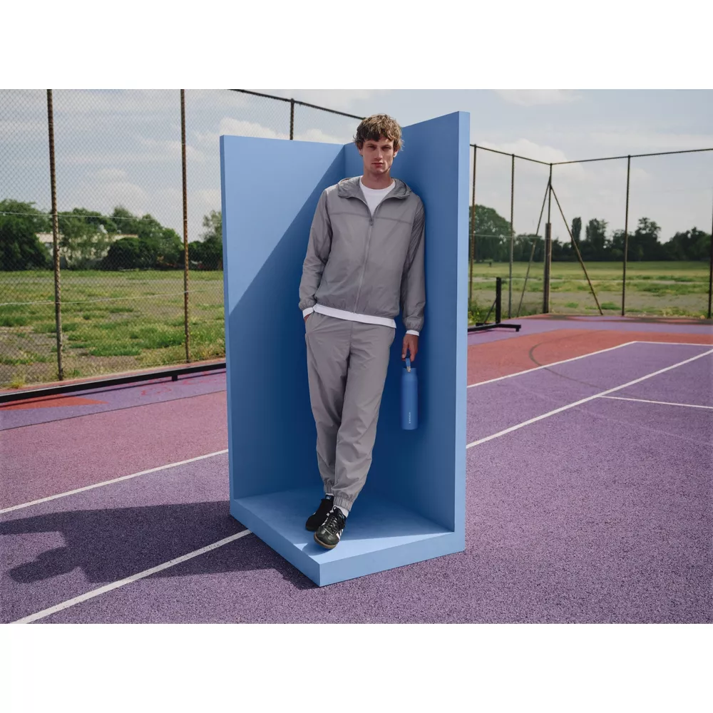 Ein Mann in grauem Trainingsanzug steht in einer blauen Ecke mit einer blauen Wasserflasche.