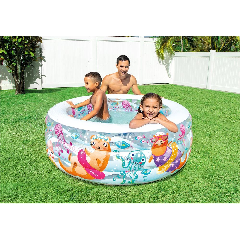 Ein Mann und zwei Kinder planschen in einem aufblasbaren Pool mit Meeresmotiven im Garten.