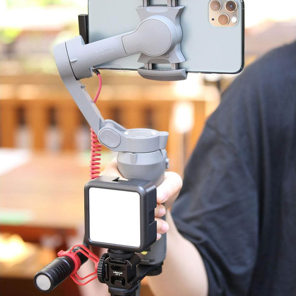 A person holds a gray Osmo phone gimbal with a light and microphone attachment.