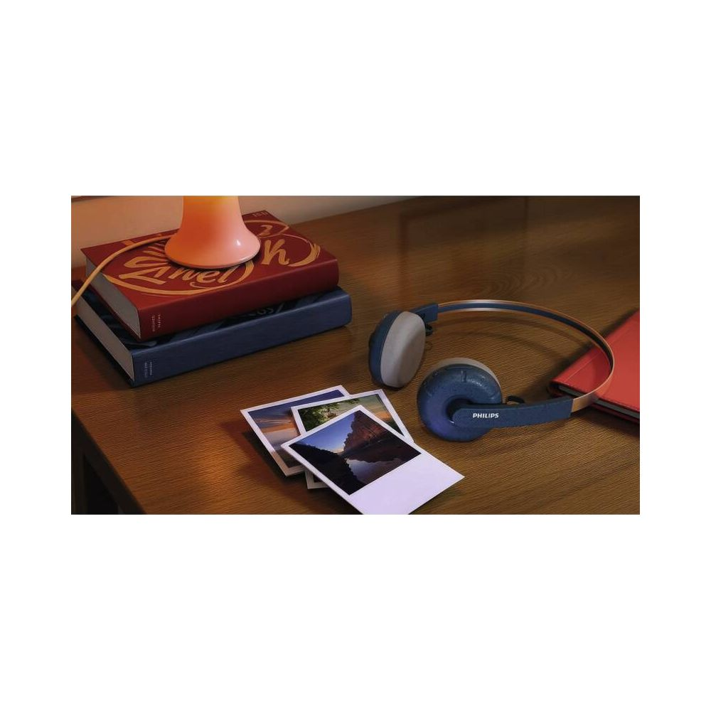 Un casque Philips bleu repose sur une table en bois à côté de livres et de photos.