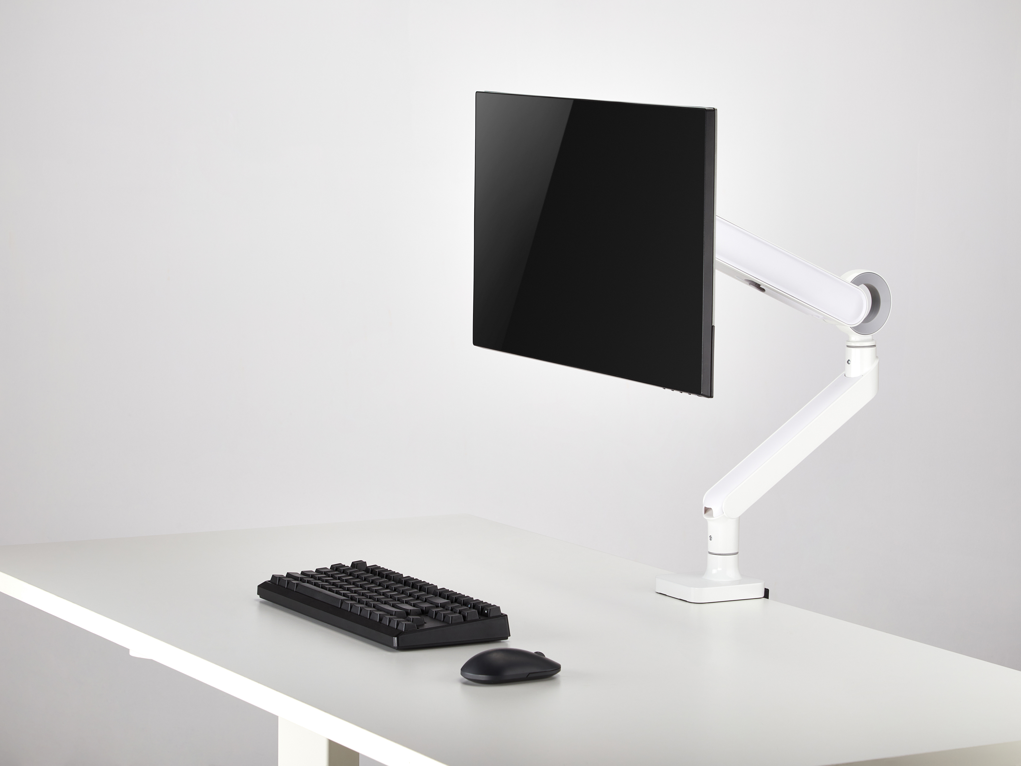 Ein schwarzer Monitor auf einem weißen Schwenkarm steht auf einem weißen Schreibtisch.