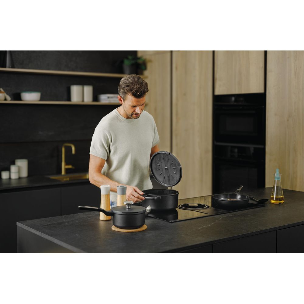Man in light clothing cooks in a modern kitchen with black pots.