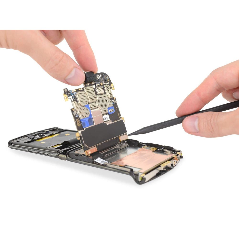 Dłonie rozkładają smartfon leżący na stole. Płytka drukowana jest wyjmowana.