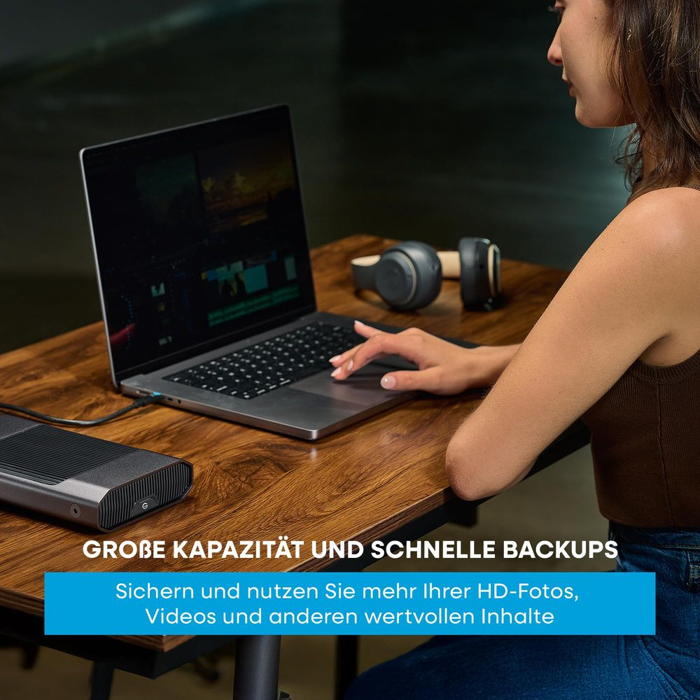 Kobieta używa laptopa, obok dysk zewnętrzny i słuchawki.