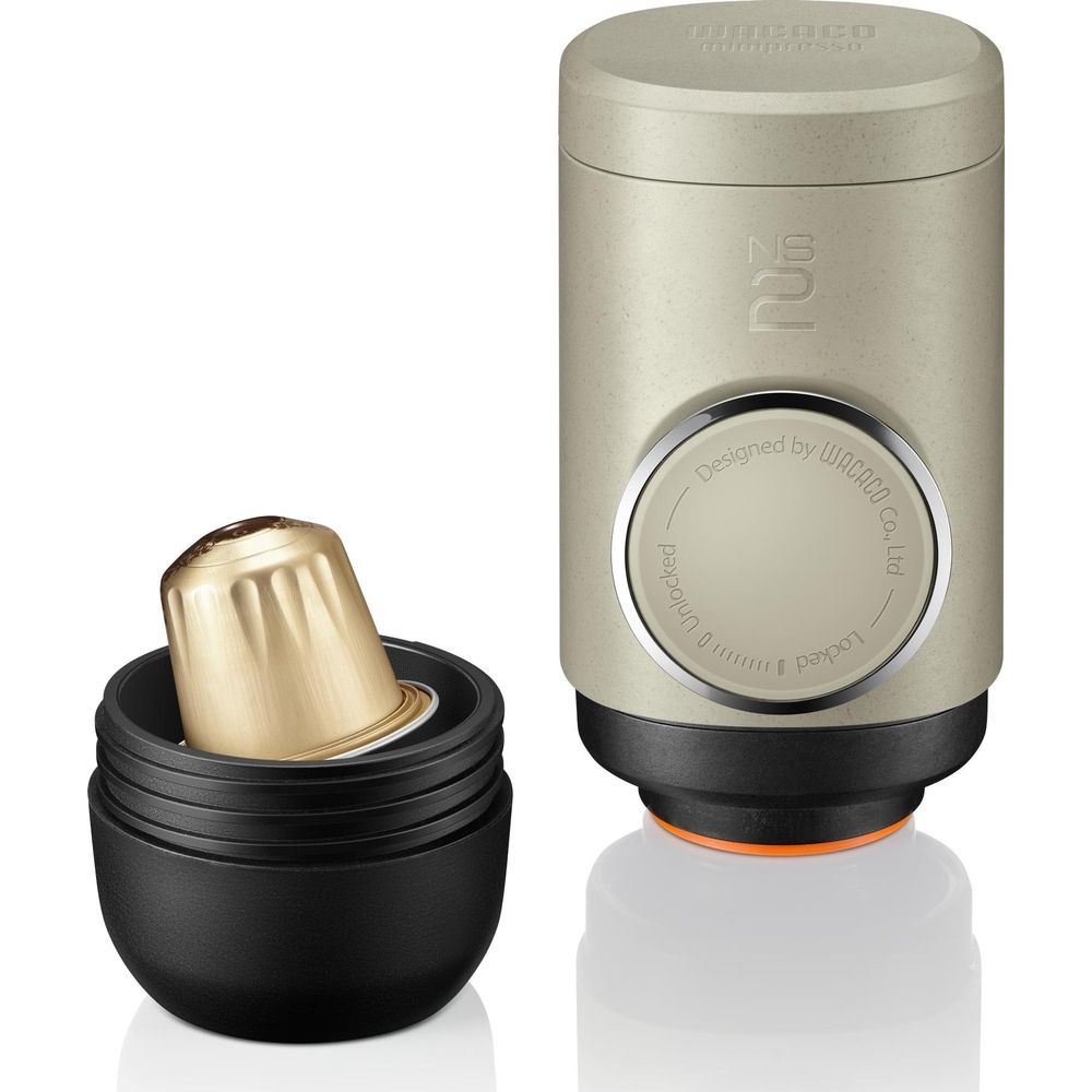Ein goldener Kaffeepod sitzt in einem offenen schwarzen Behälter neben einem beige-farbenen Gerät.