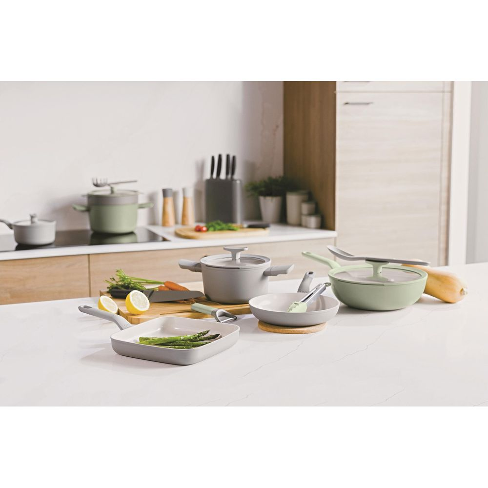 Gray and green cookware with vegetables on a kitchen counter.