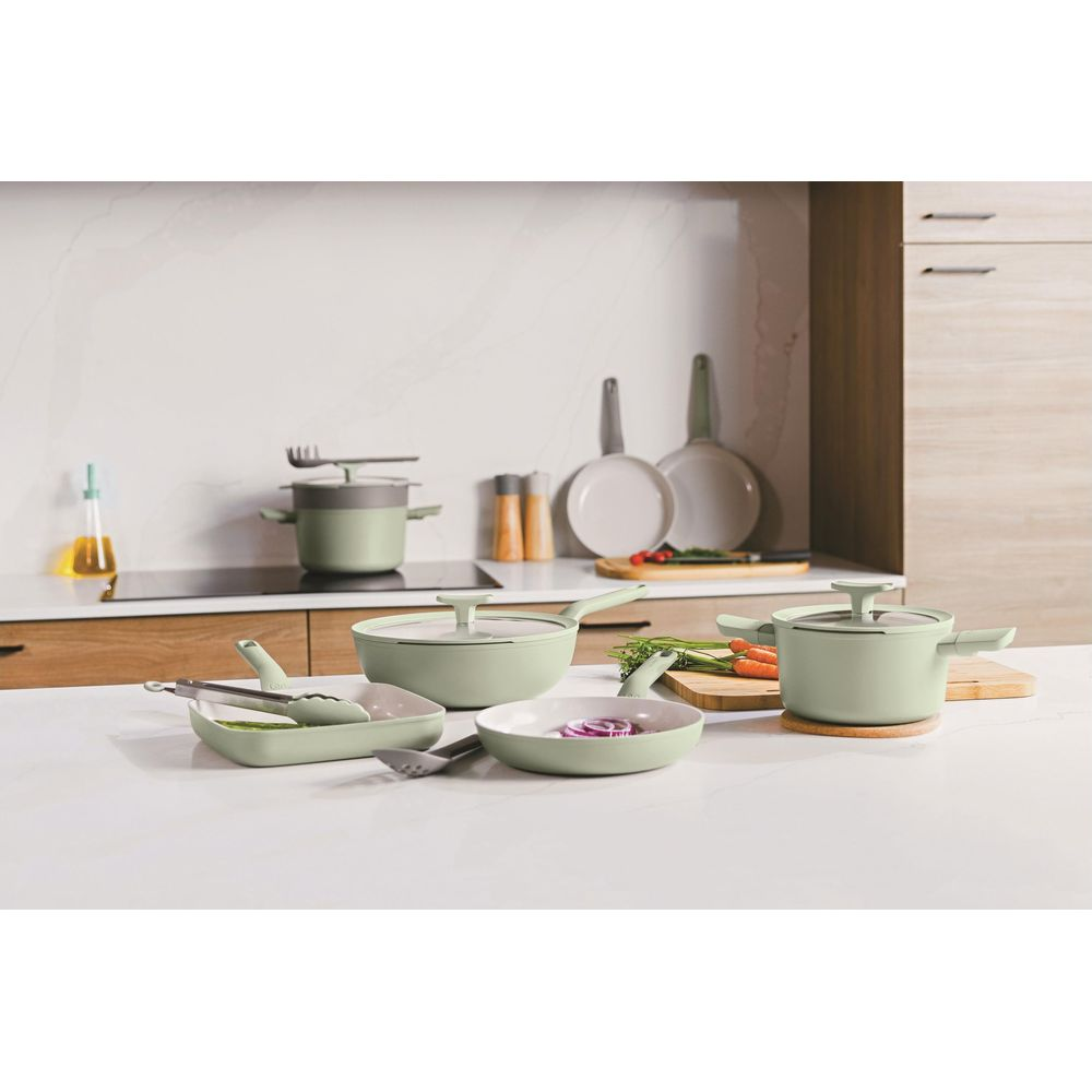 A set of sage green cookware is arranged on a white countertop with ingredients.