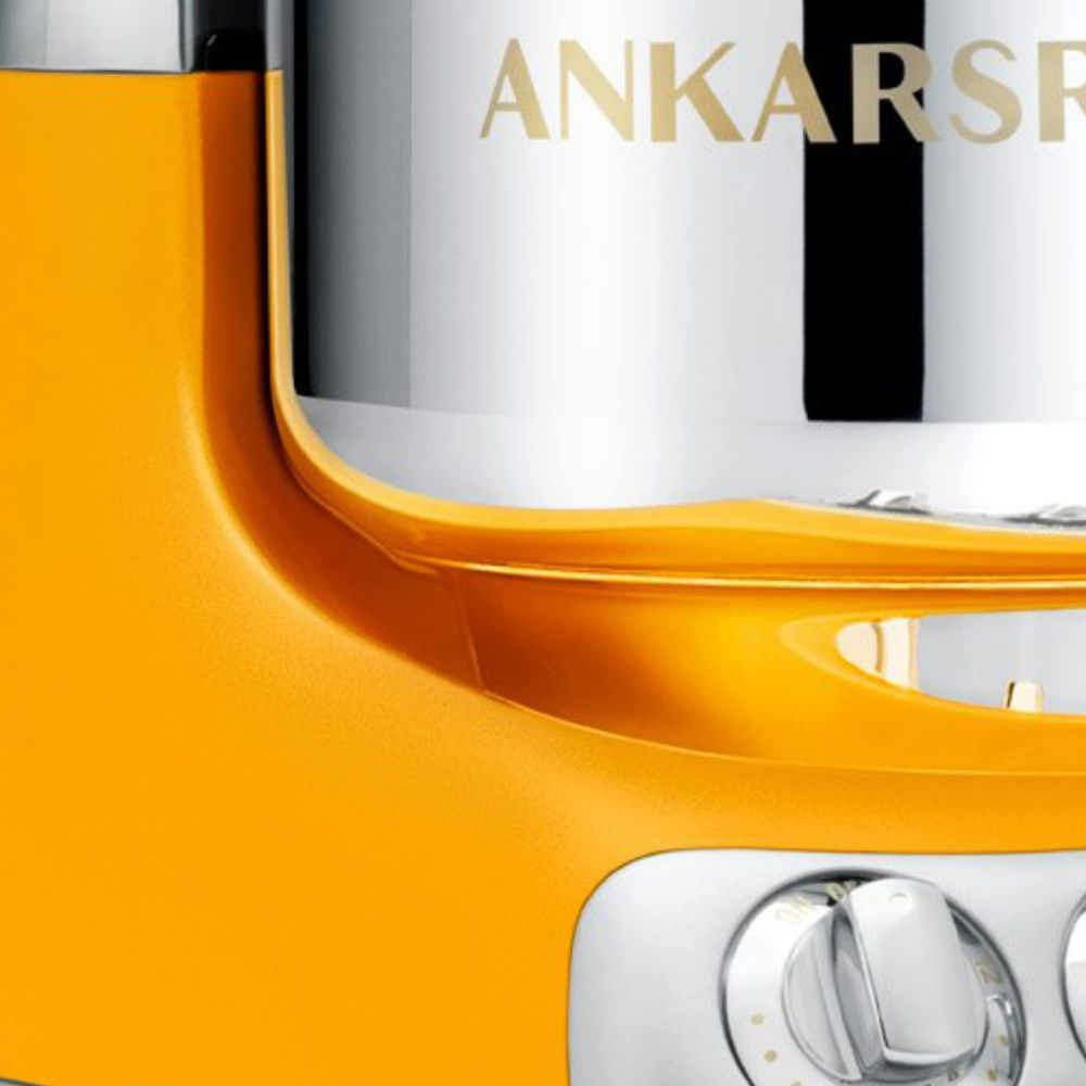 Orangefarbener Mixer mit silbernem Zylinder und goldenem Schriftzug.