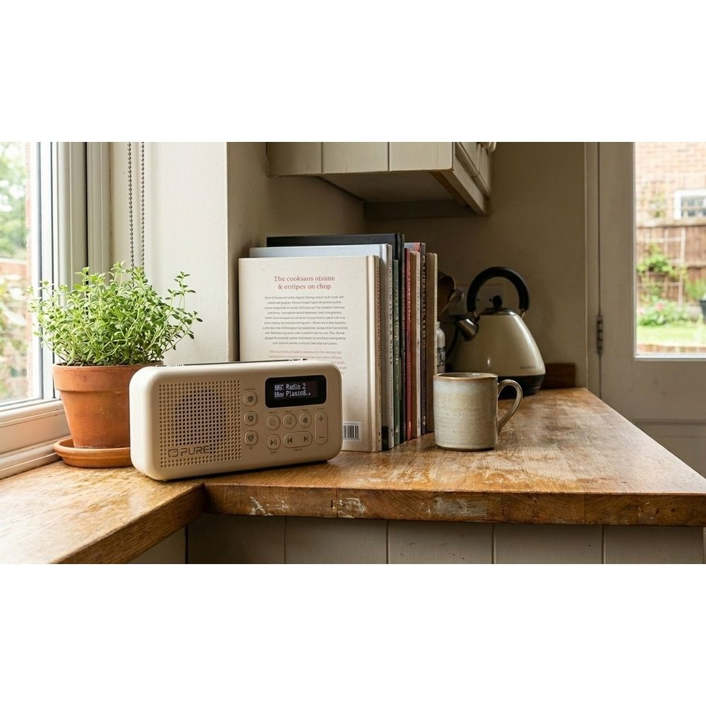 Una radio digitale beige su un bancone di legno accanto a libri e una pianta.