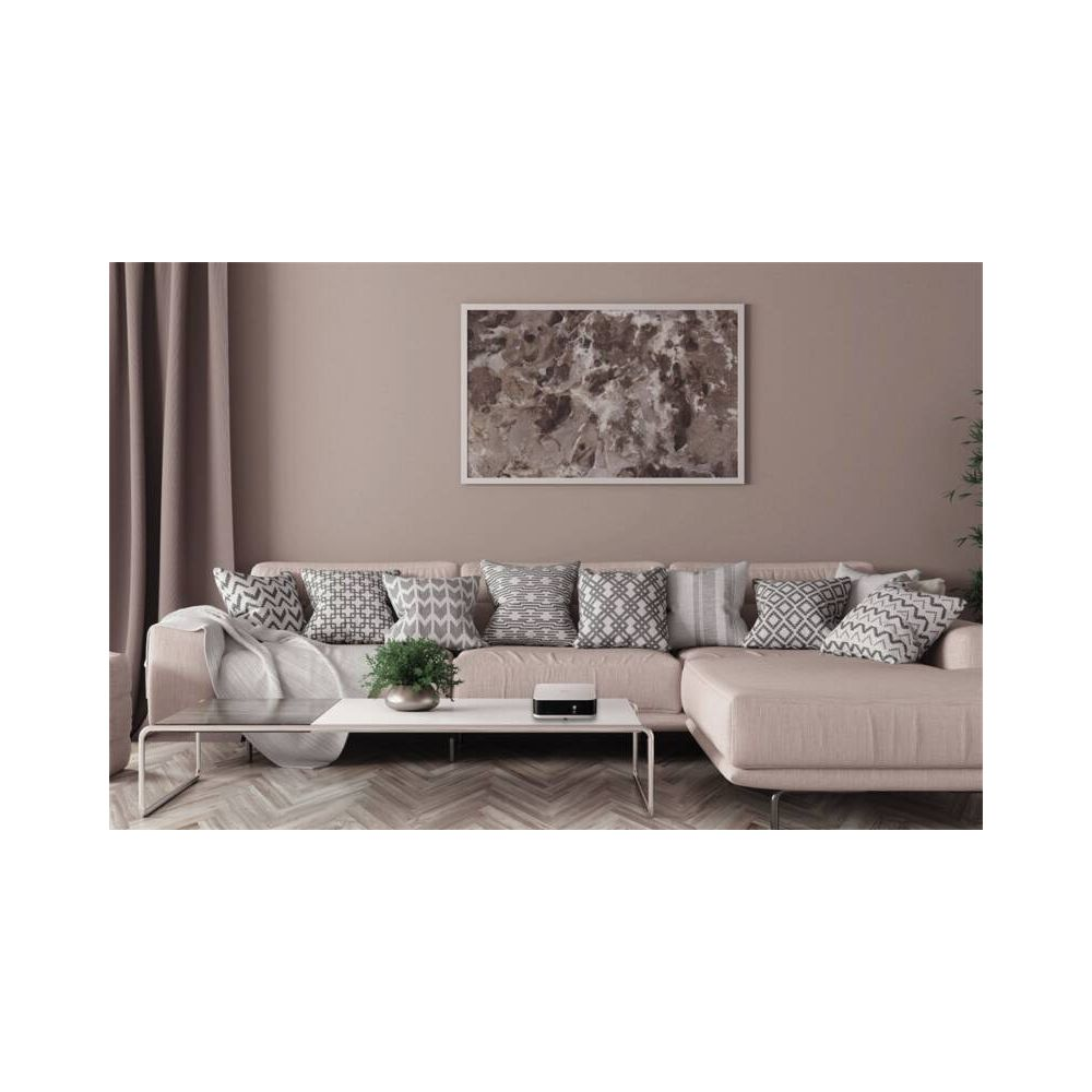Un canapé d'angle beige avec des coussins à motifs et une table basse avec une plante et un appareil.