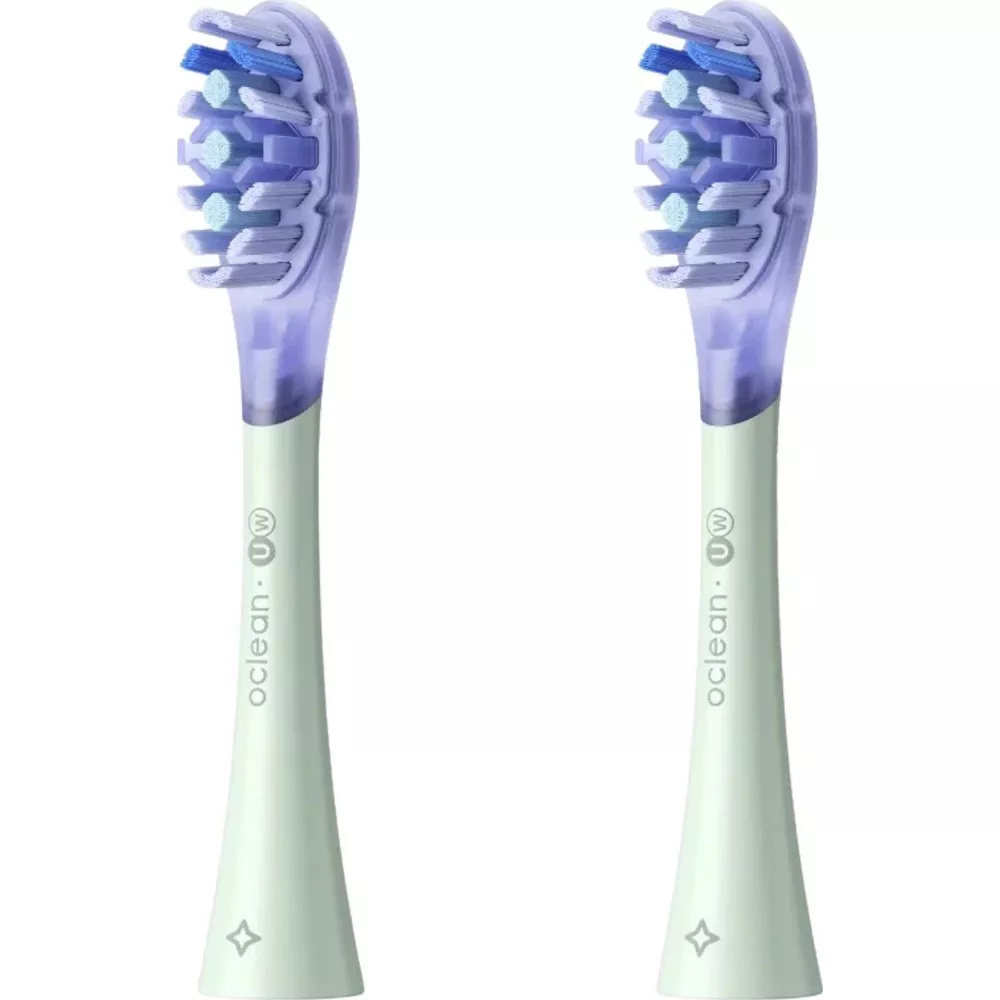 Two light green electric toothbrush heads with purple translucent tops, side by side.