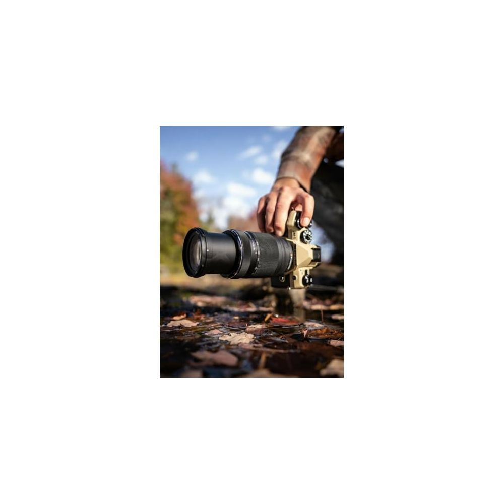 Een hand houdt een camera met een lange lens boven bladeren en water.