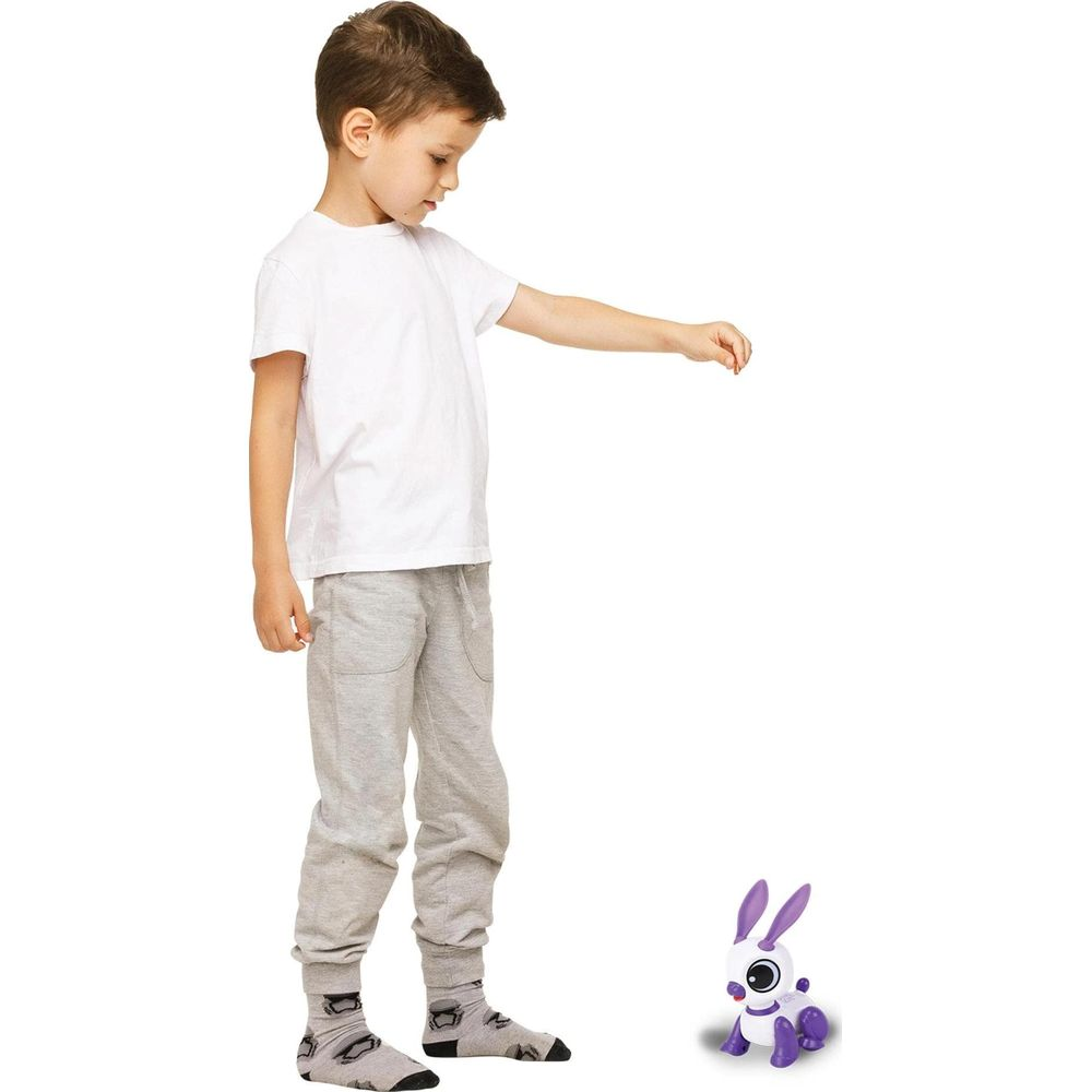 Ein Junge in einem weißen T-Shirt und Jogginghose interagiert mit einem kleinen lila Roboterhasen.