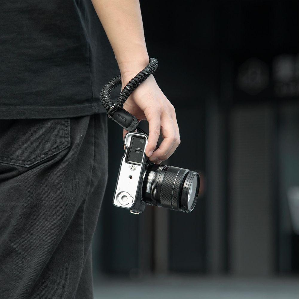 A hand holds a camera with a black wrist strap attached.