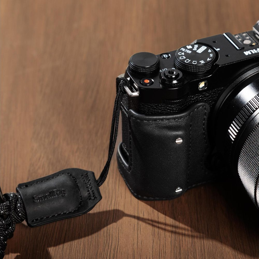 A black camera with a leather case and strap on a wooden surface.