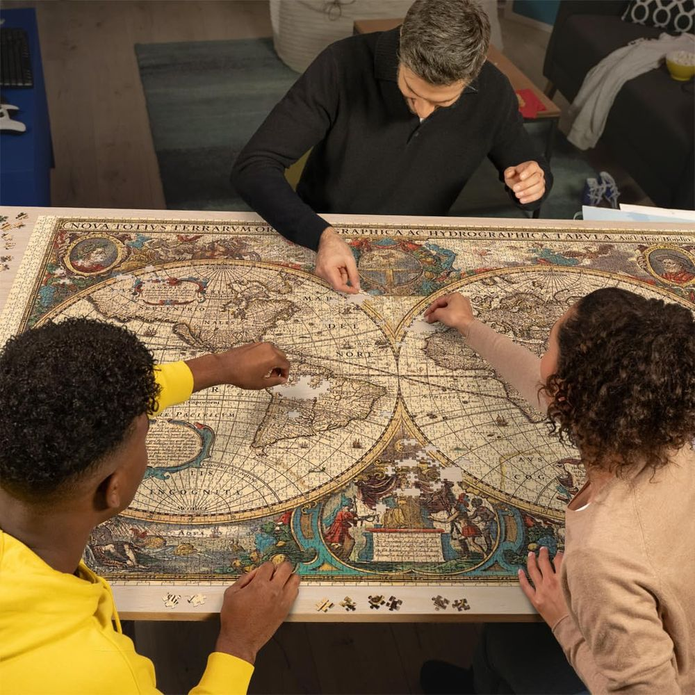 Trois personnes assemblent un grand puzzle de carte du monde sur une table en bois.