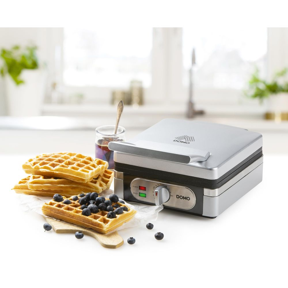 Una piastra per waffle argentata con waffle pronti, mirtilli e marmellata.
