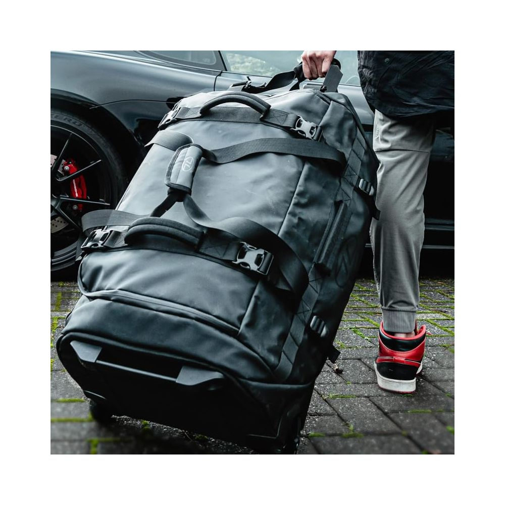 Eine Person zieht eine große schwarze Reisetasche mit Rädern neben einem schwarzen Auto.
