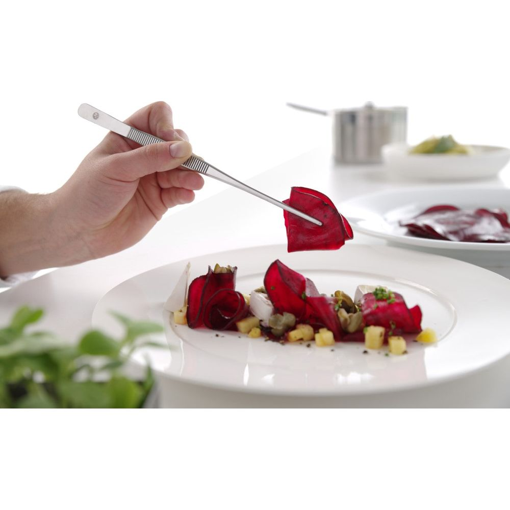 Uno chef usa una pinzetta per posizionare fette di barbabietola rossa su un piatto.