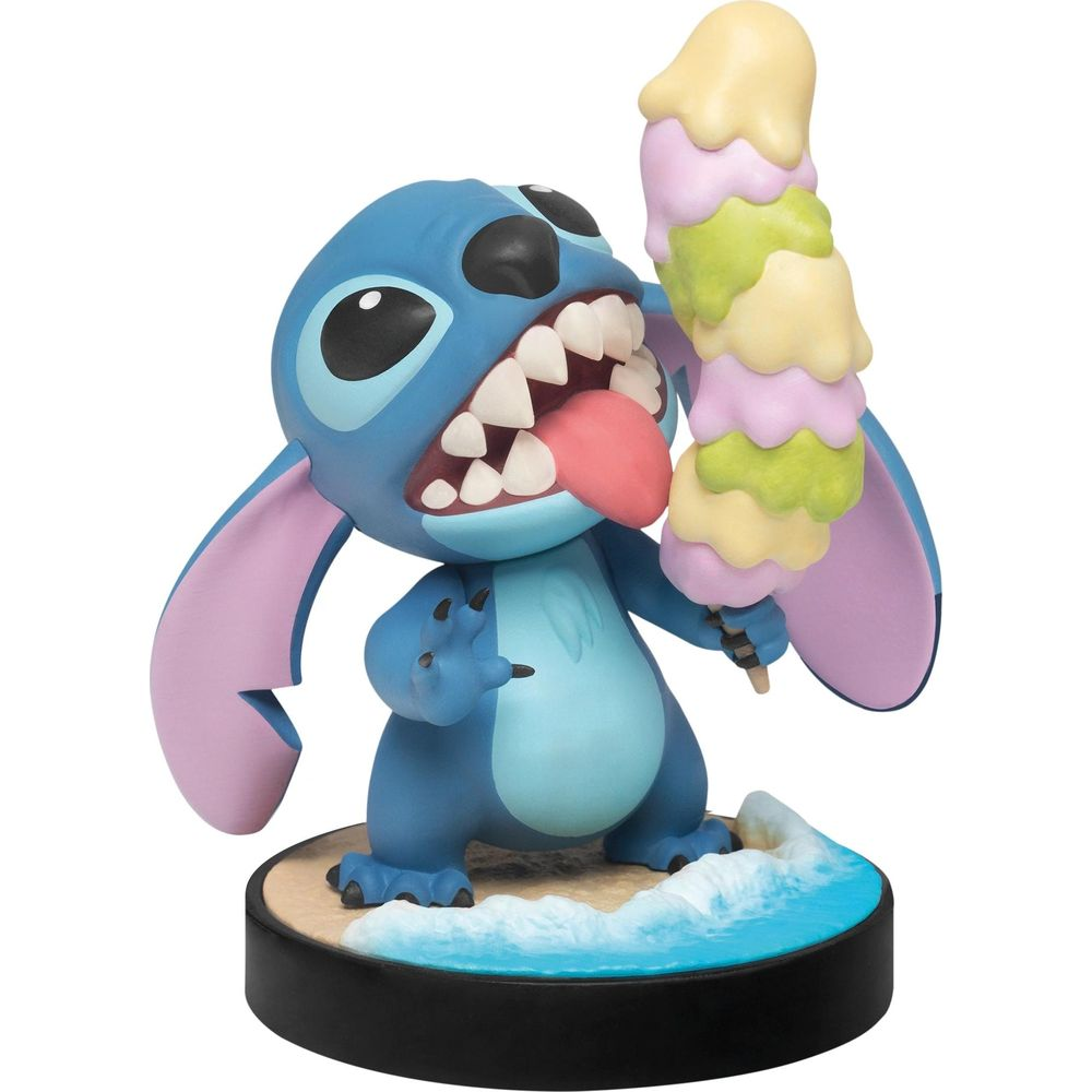 Une figurine bleue de Stitch mangeant une glace multicolore sur un socle sable et mer.