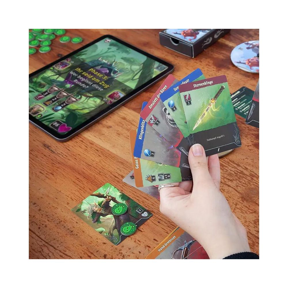 Brettspiel mit Tablet und Karten auf Holztisch. Eine Hand hält Spielkarten.