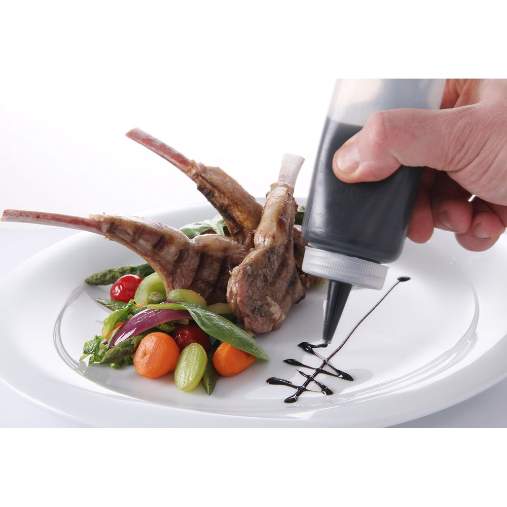 Una mano usa una bottiglia squeeze per versare la salsa su un piatto di costolette d'agnello e verdure.