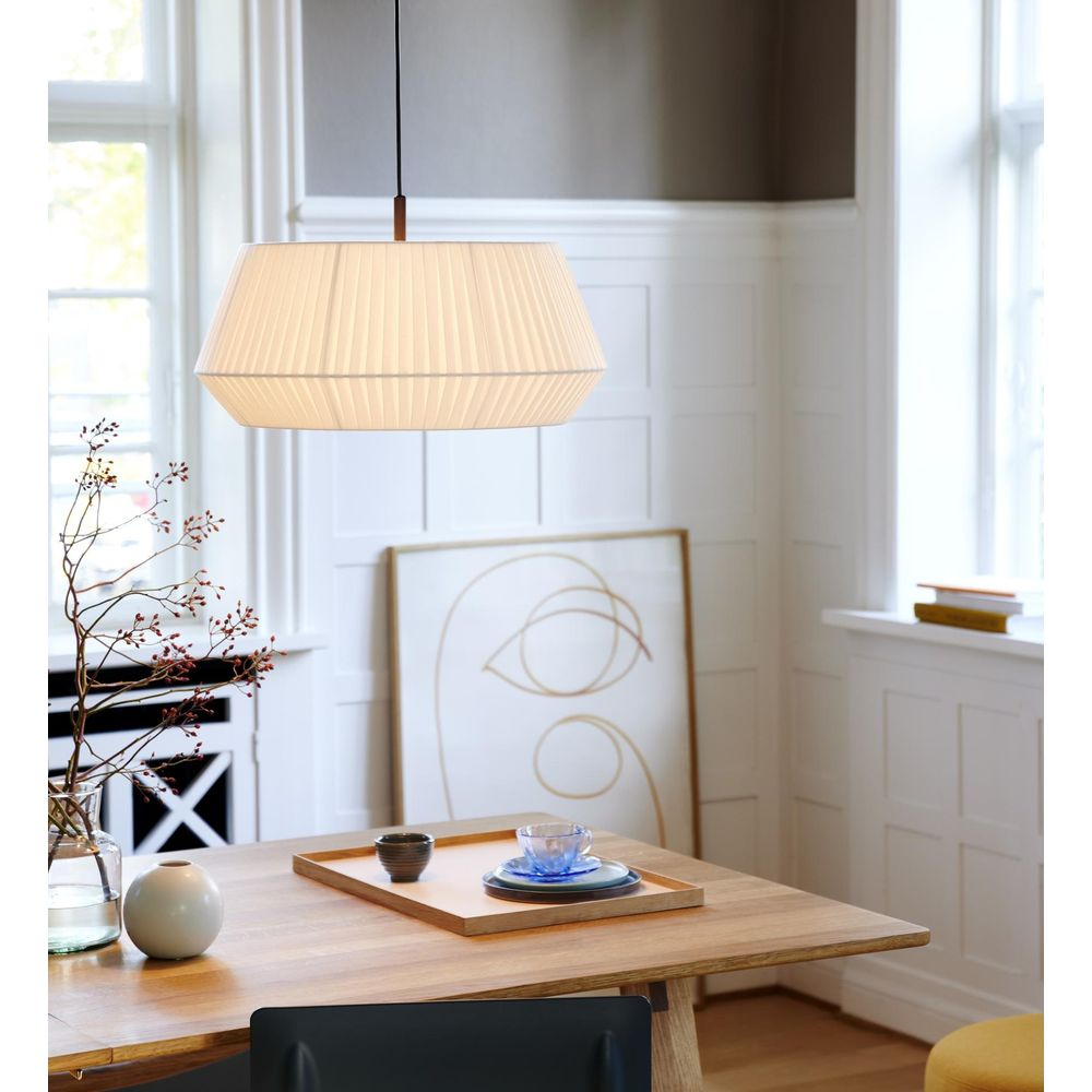 Un abat-jour plissé est suspendu au-dessus d'une table en bois avec un vase et un plateau.