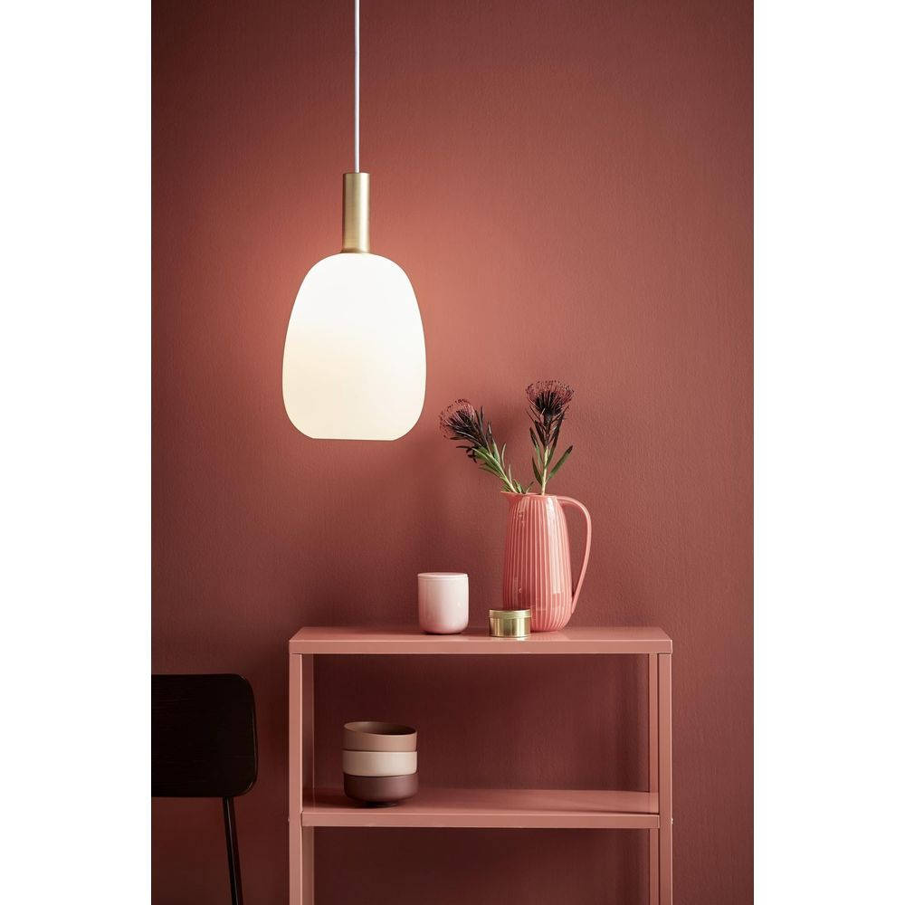 Lampe suspendue au-dessus d'une étagère rose avec vase et bougies.