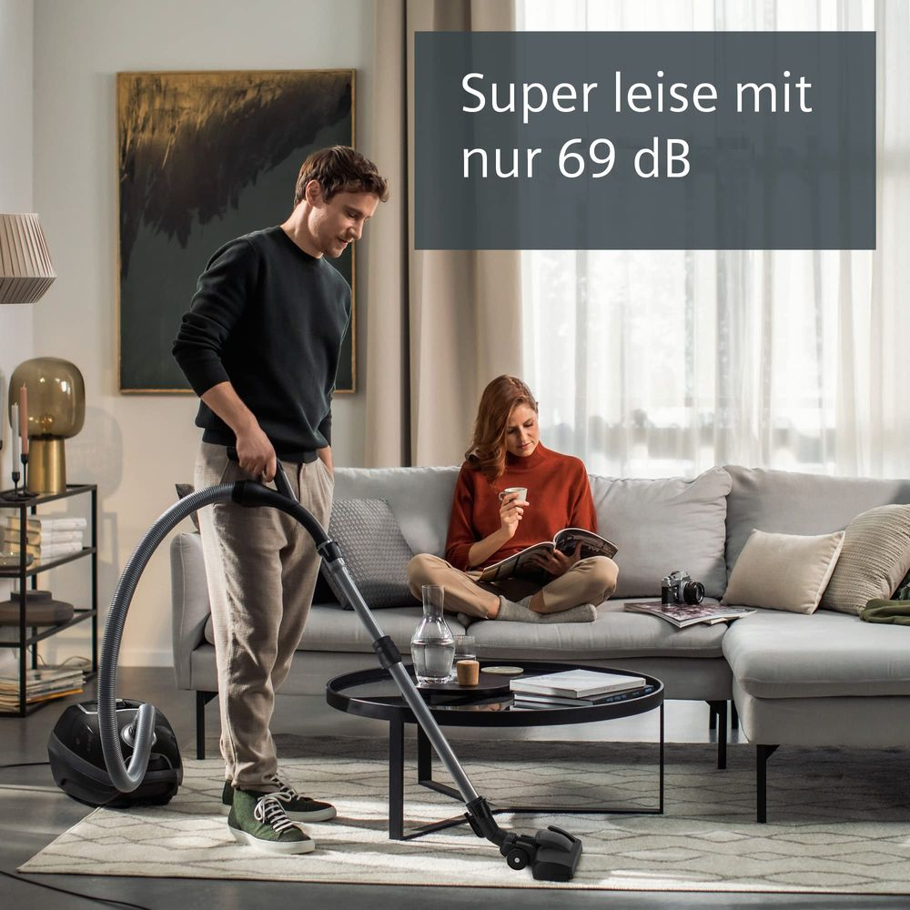 Mężczyzna odkurza, kobieta czyta na sofie. Cicho 69 dB.
