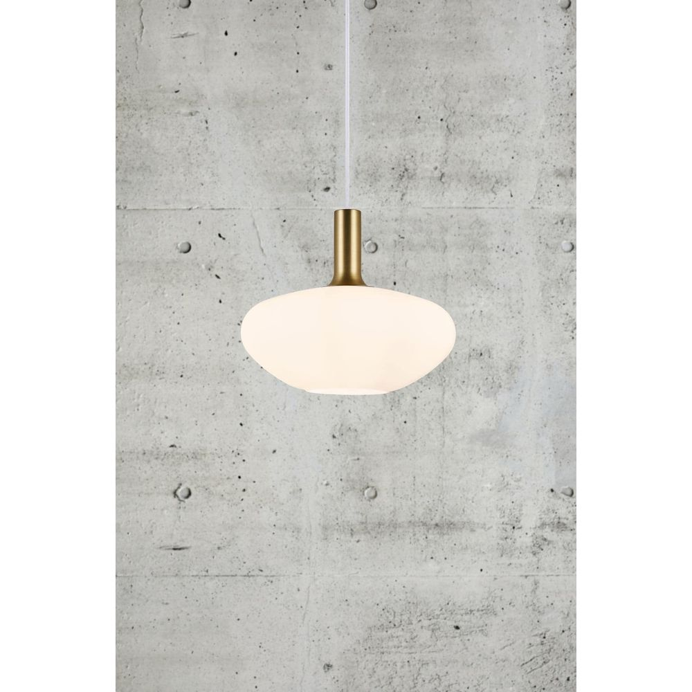 Un plafonnier ovale blanc avec un luminaire doré est suspendu devant un mur de béton.
