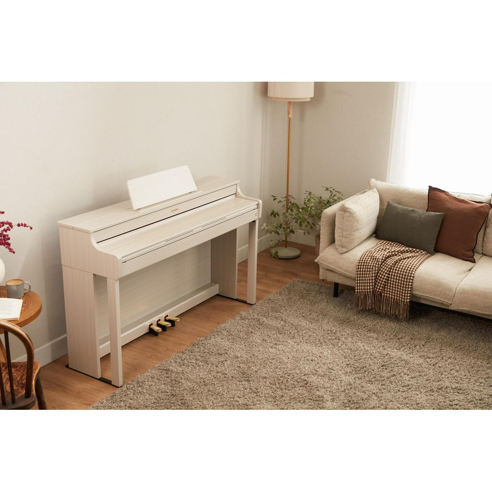 Un piano de couleur claire se trouve dans un salon à côté d'un canapé, d'un tapis et d'une lampe.