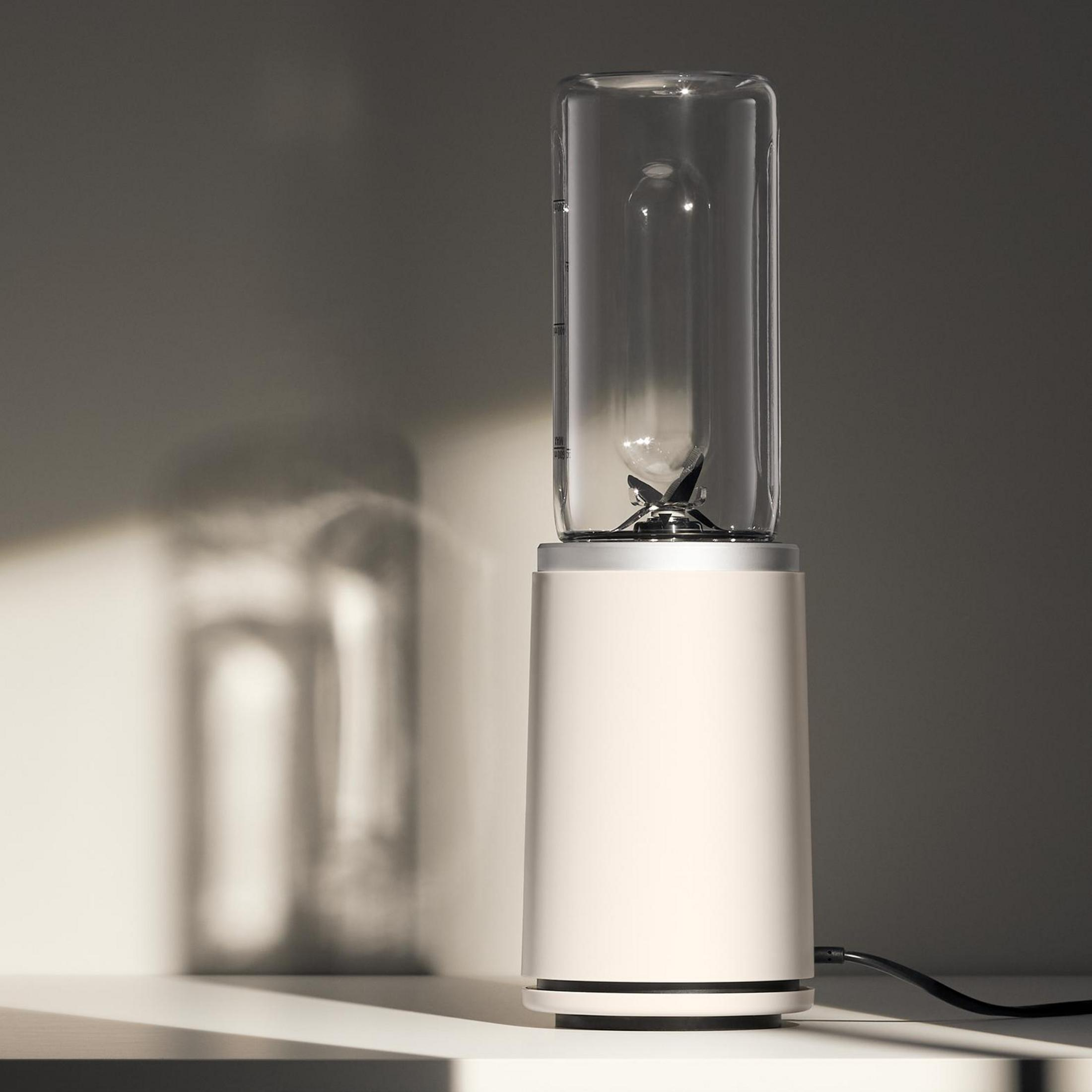 Ein eleganter, cremefarbener Personal Blender mit Glasbehälter und Metallklingen steht auf weißer Fläche.