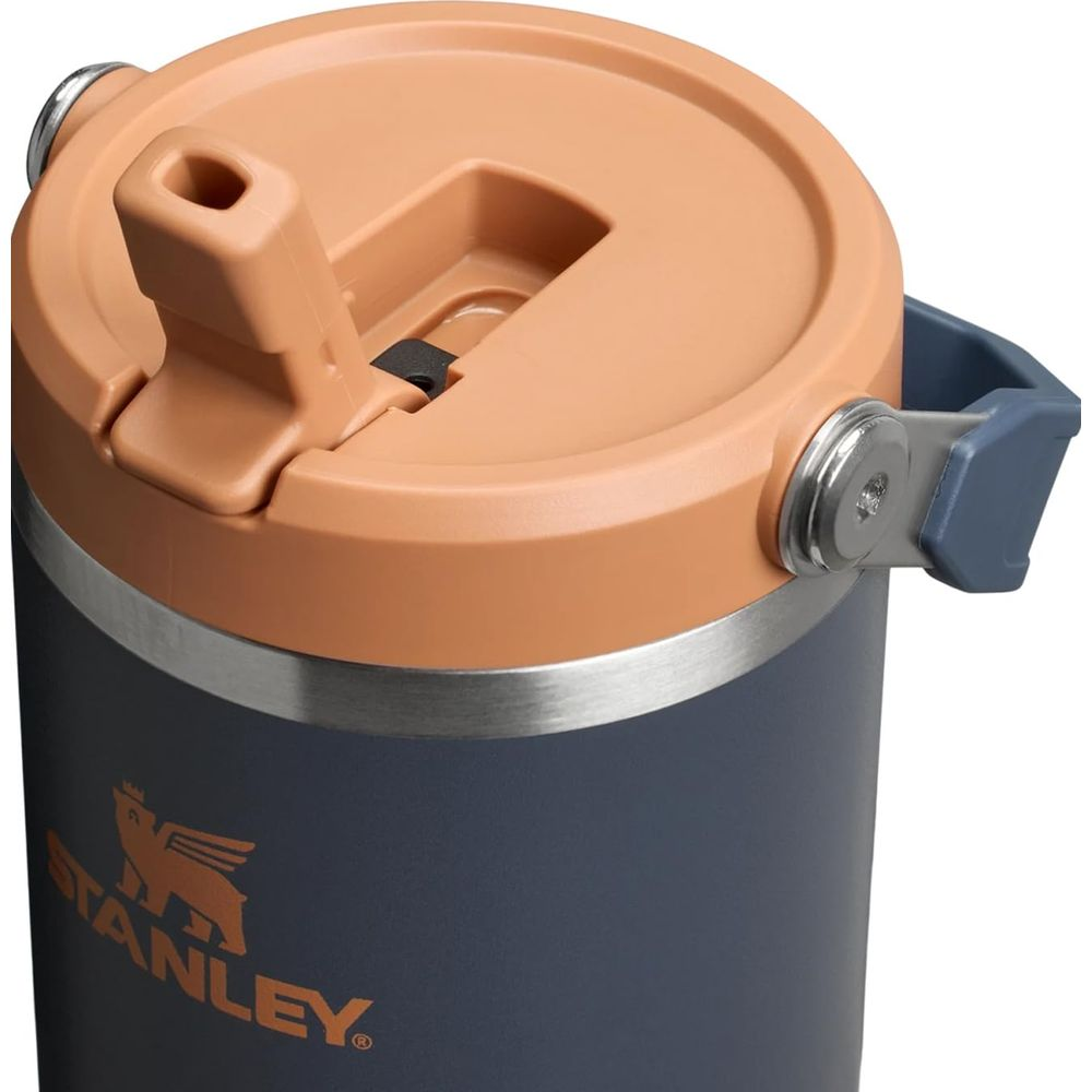 Turuncu kapaklı ve katlanır tutamaklı koyu gri termos bardak. Stanley logosu görünür.